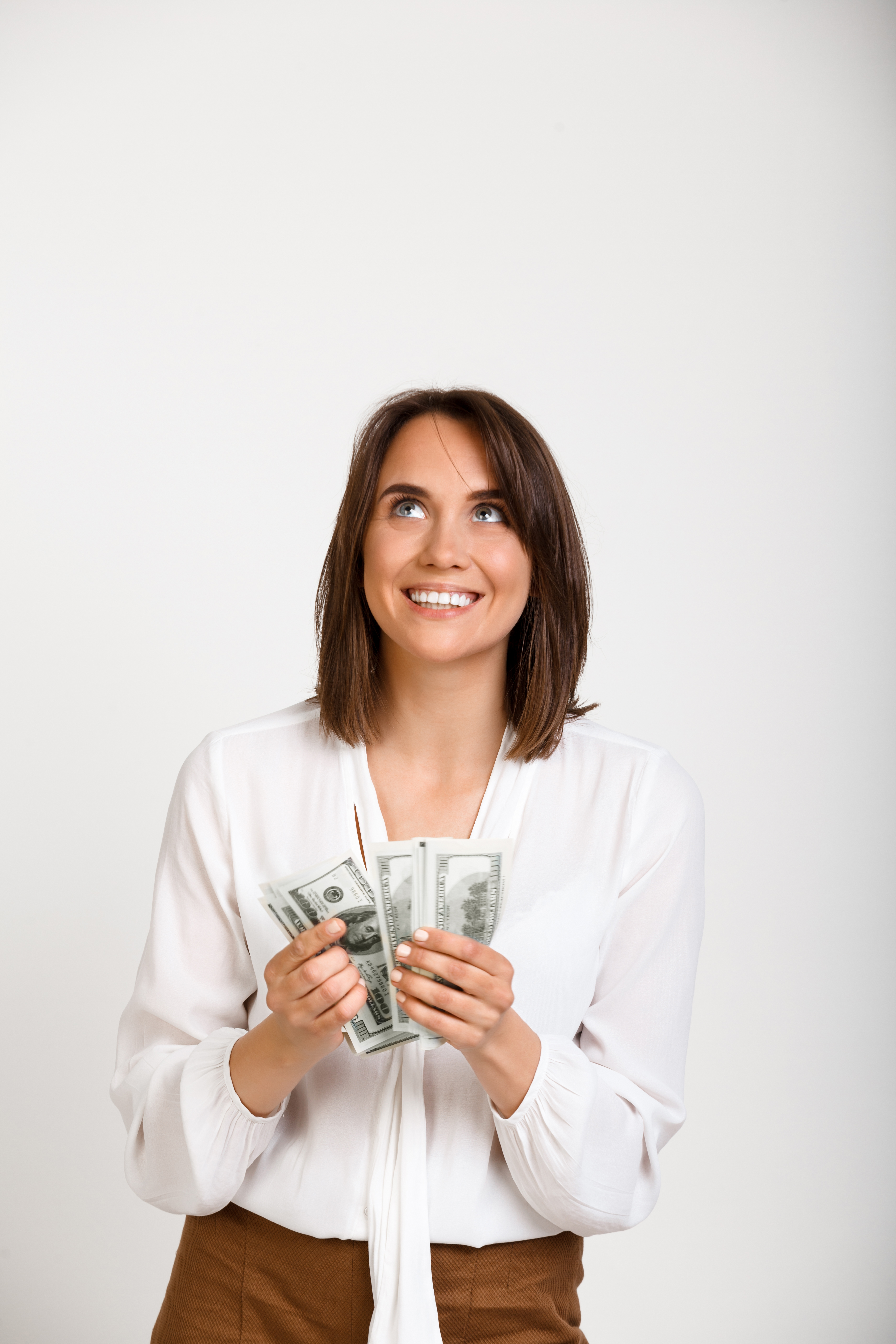 Portrait of young successful business woman smiling, holding money, over white background.