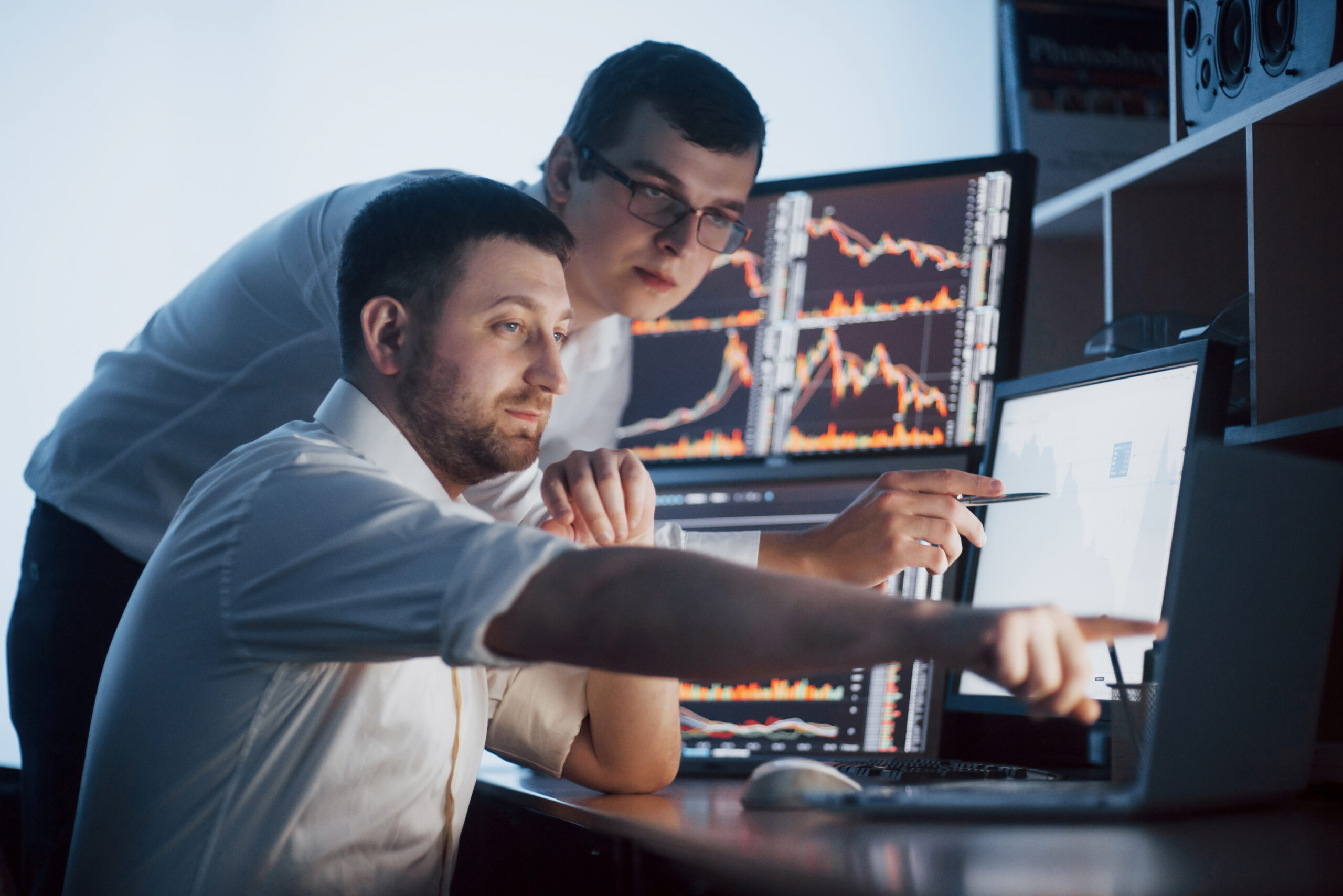 Team of stockbrokers are having a conversation in a dark office with display screens. Analyzing data, graphs and reports for investment purposes. Creative teamwork traders.