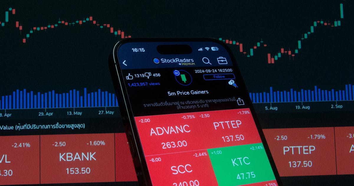 Celular com app de cotações de ações e gráfico ao fundo representando ações ON e PN