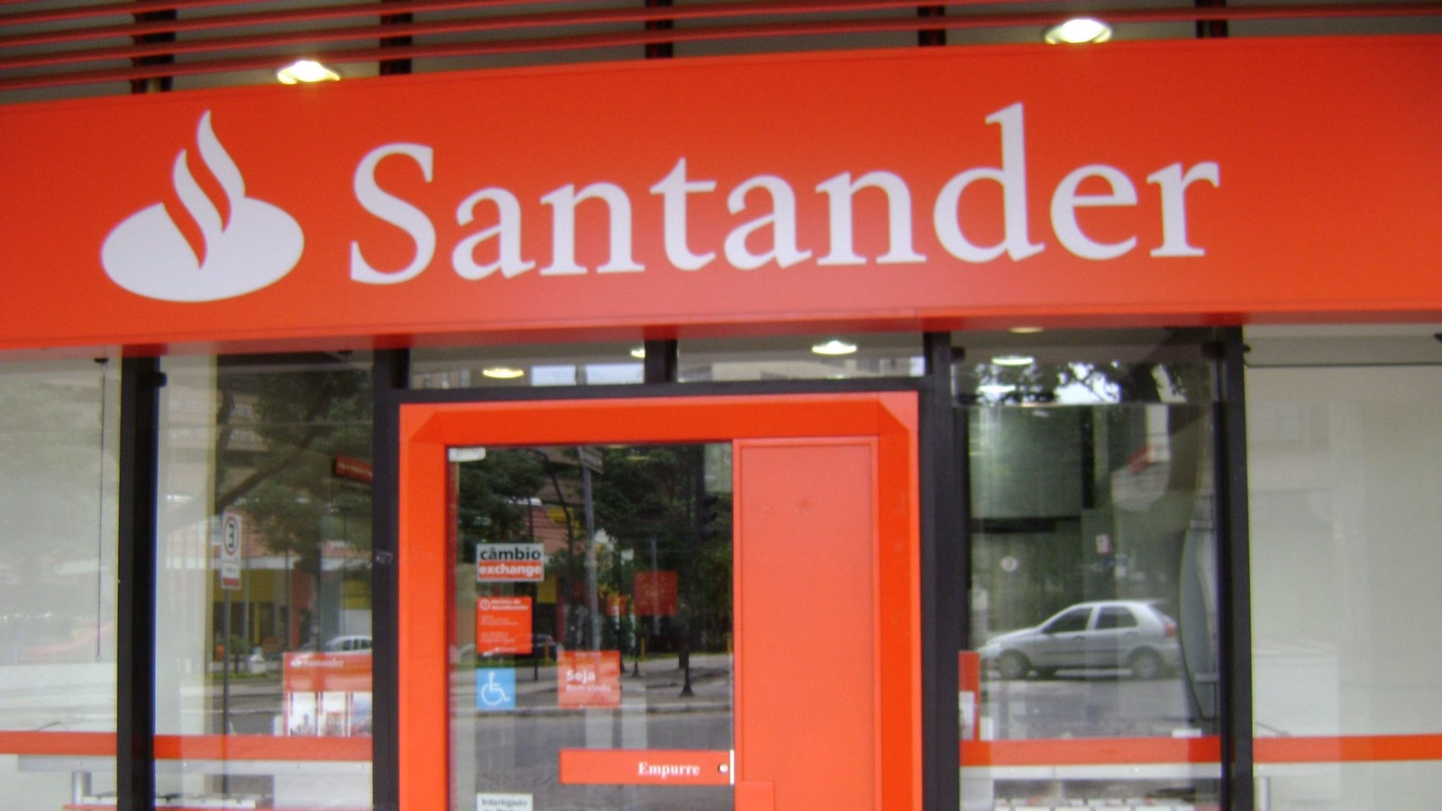 Fachada de agência do Santander com o logotipo vermelho e branco acima da porta