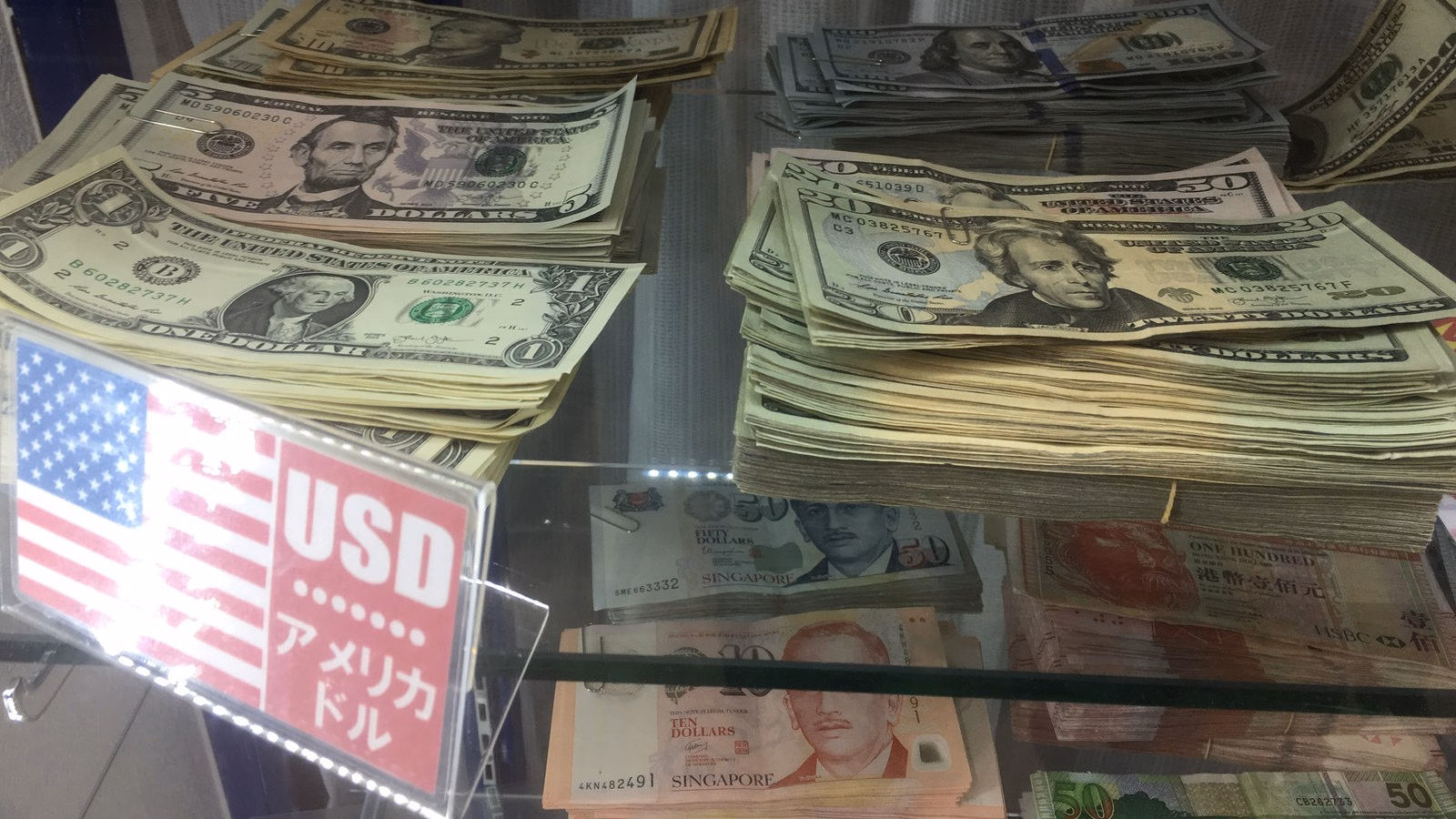 Maços de notas de dólar expostos numa vitrine de casa de câmbio, com placa USD